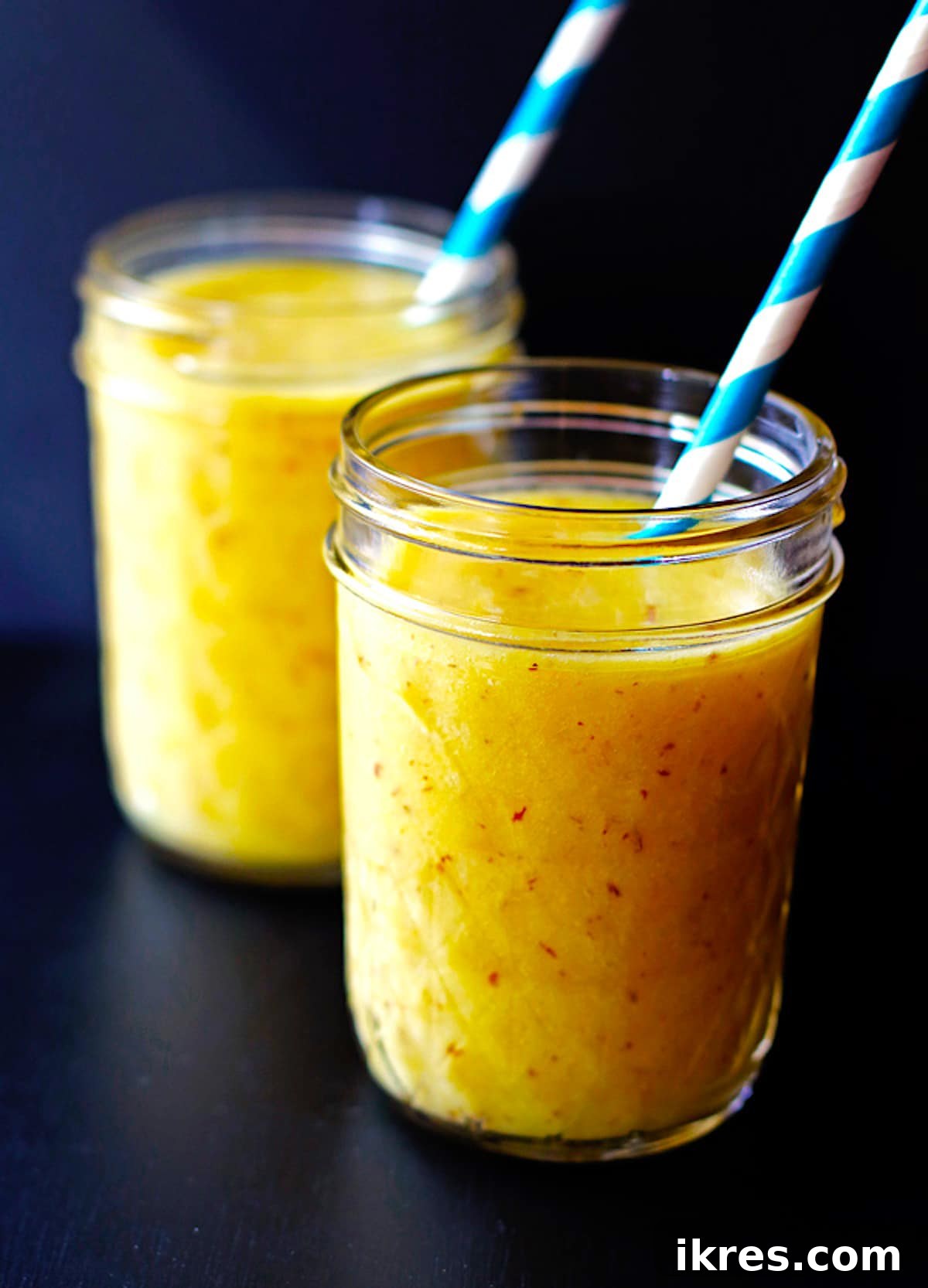 Two glass jars filled with a vibrant pineapple, mango, and banana smoothie, showcasing the refreshing and creamy texture.