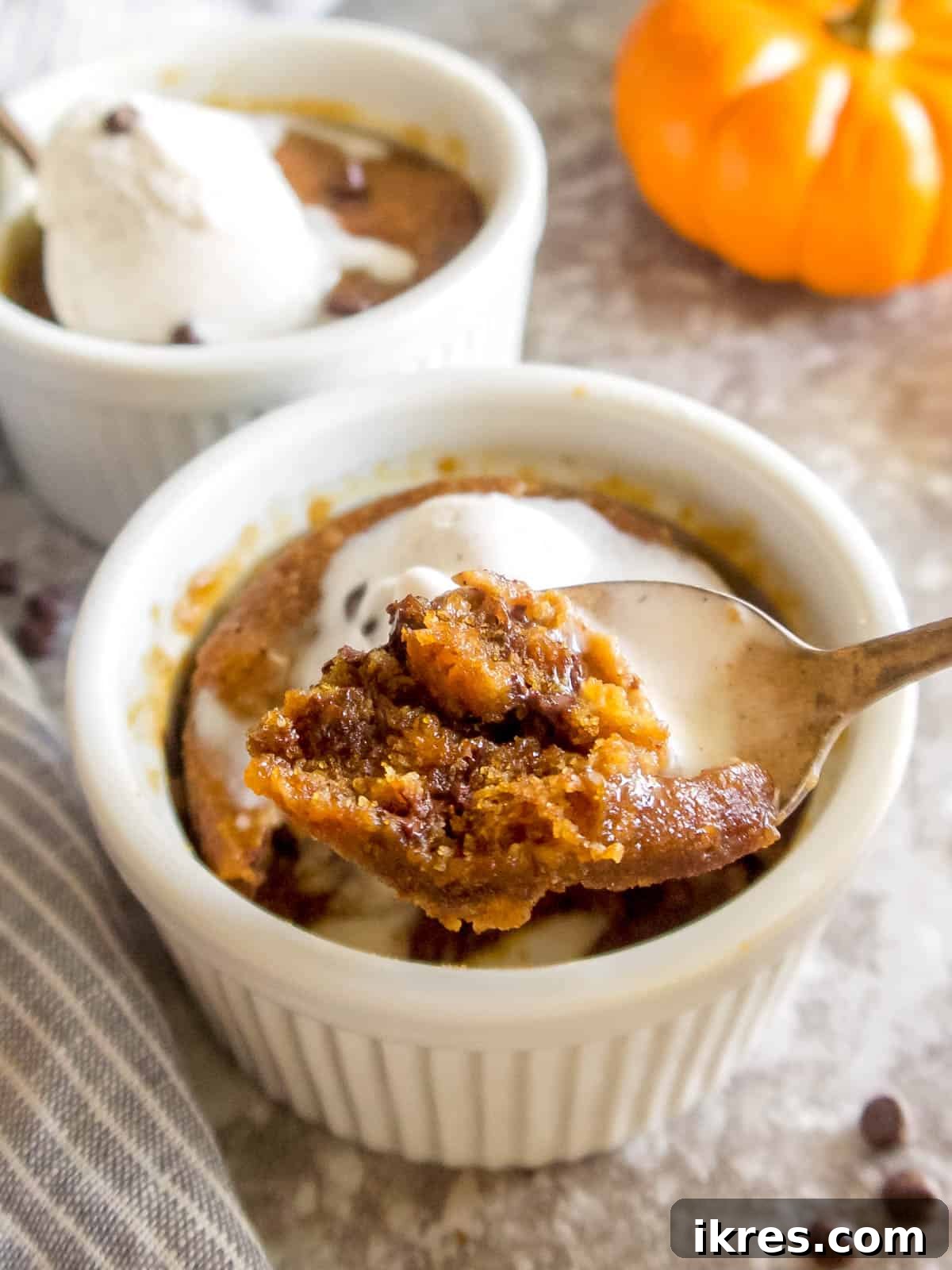 Easy Paleo Pumpkin Spice Mug Cake 3 A close-up shot of a spoon taking a bite from a pumpkin chocolate chip mug cake, showcasing its soft, gooey texture and melted chocolate chips.