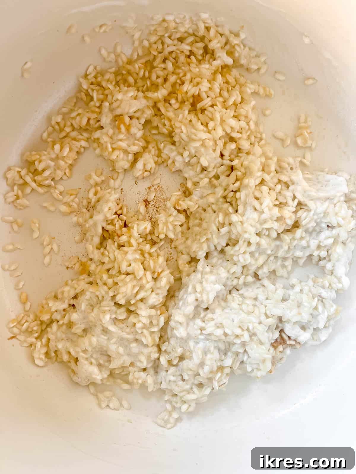 Thick coconut cream being stirred into the toasted Arborio rice in a pot.