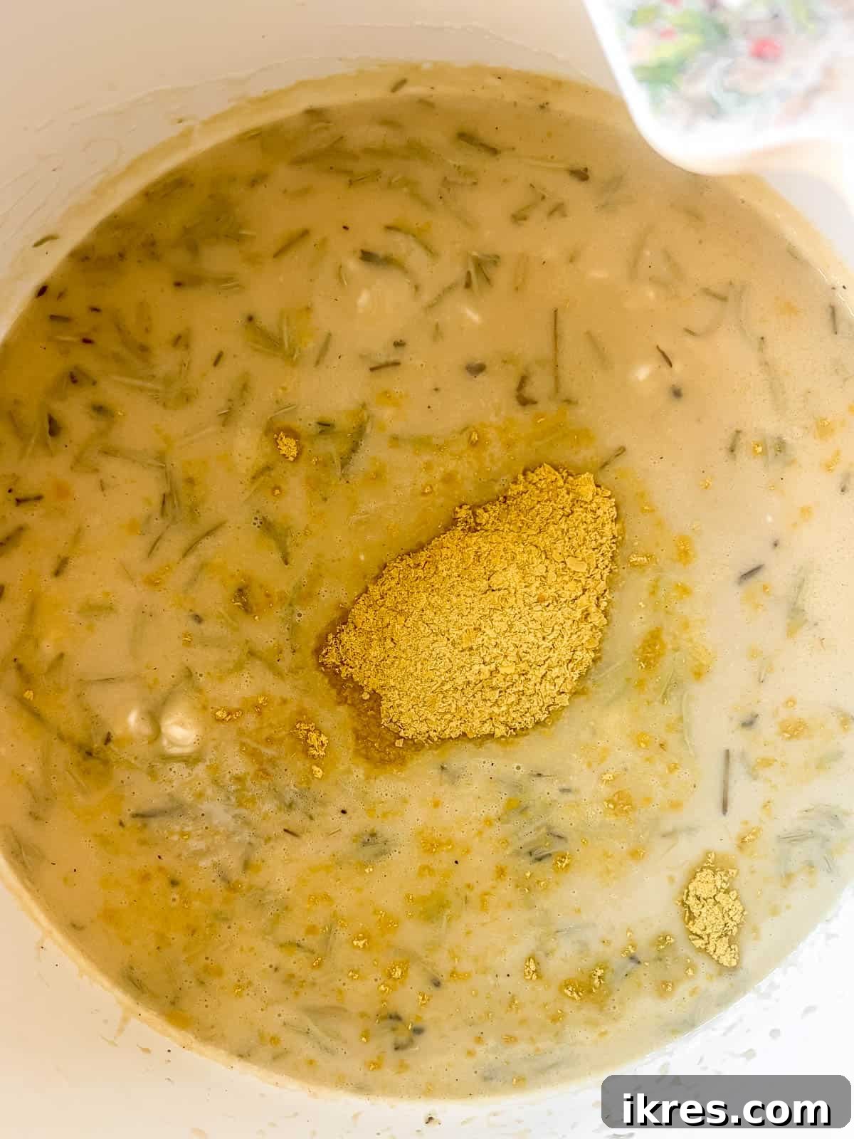 The risotto cooking in a pan, with more broth and nutritional yeast being stirred in to create a creamy consistency.