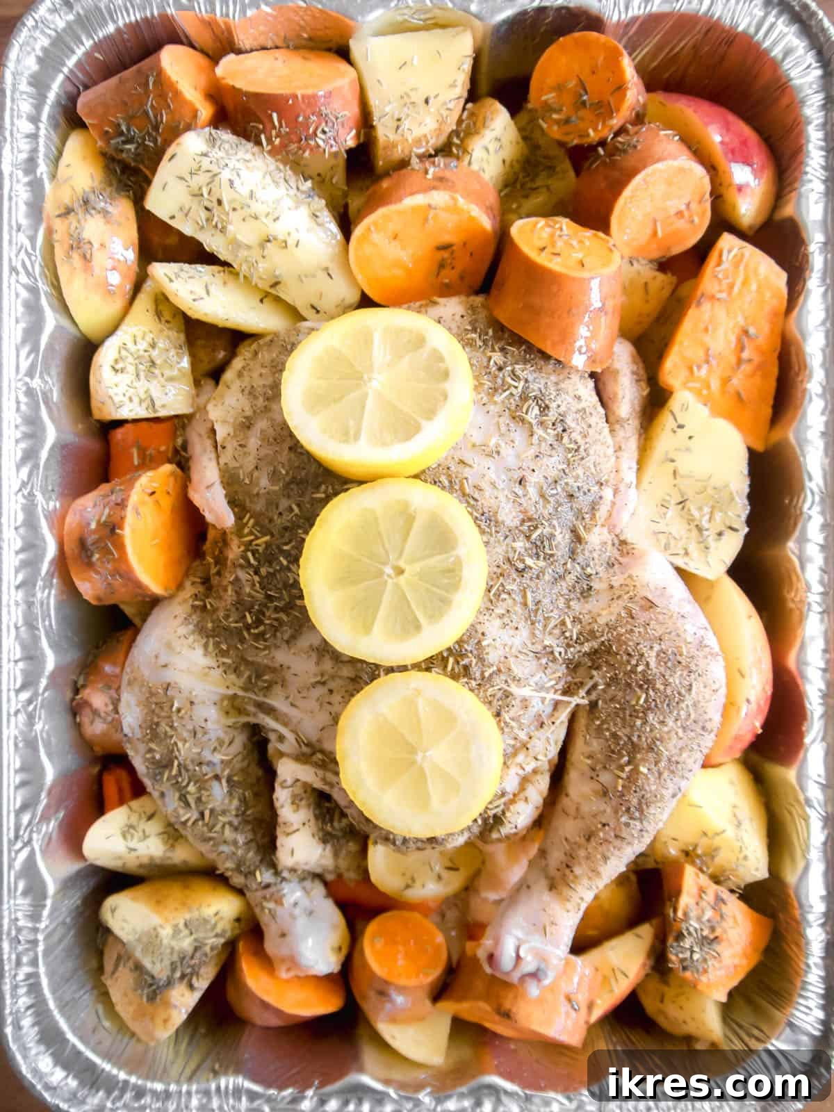 Golden Roast Chicken with Apples and Potatoes Dairy Free 7 Raw chicken surrounded by sliced potatoes, sweet potatoes, carrots, and apples in a roasting pan.
