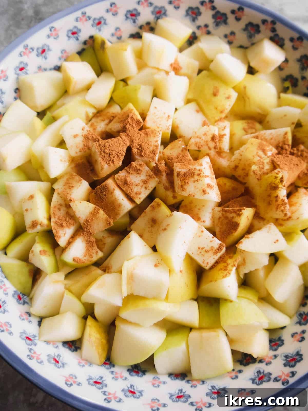 Diced apples tossed with maple syrup, lemon juice, and cinnamon, ready for initial baking in a baking dish.