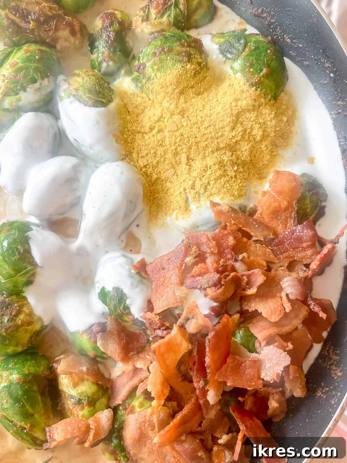 Wholesome Brussels Sprouts Bake Paleo Whole30 8 Cooked Brussels sprouts in a pan, with coconut cream, nutritional yeast, and crumbled bacon added on top, ready for mixing.