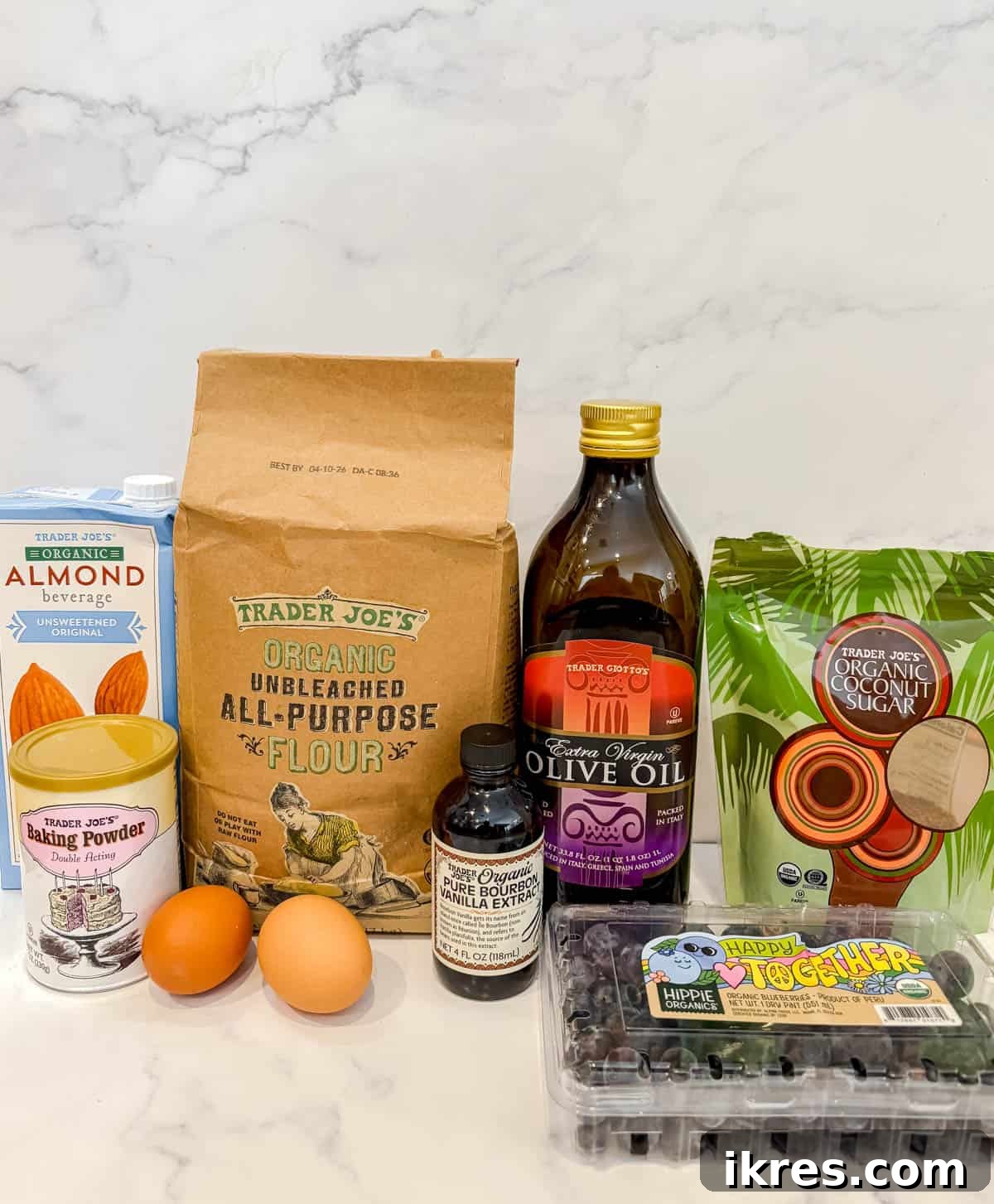 Naturally Dairy-Free Olive Oil Blueberry Muffins 3 A flat lay of ingredients laid out for making dairy-free blueberry muffins, including flour, sugar, olive oil, eggs, almond milk, and fresh blueberries.
