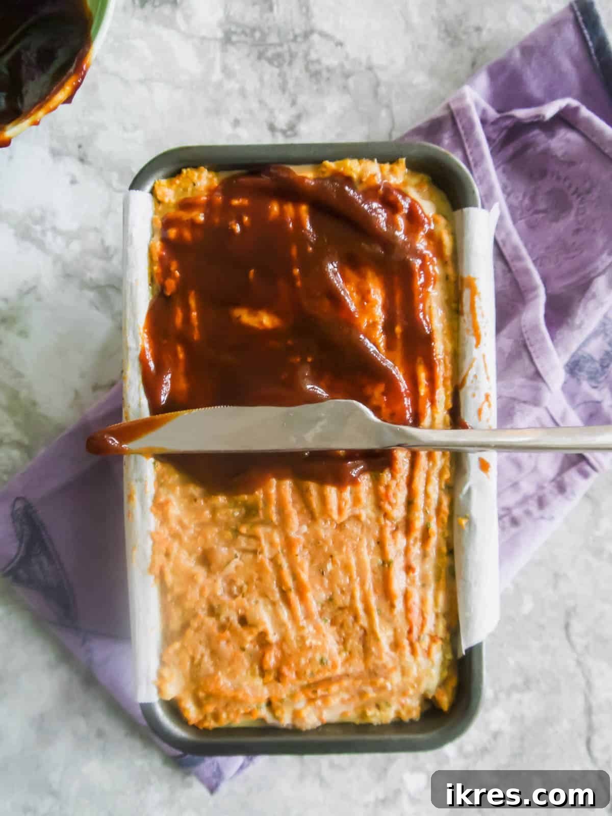 Meatloaf in a loaf tin with the ketchup molasses sauce generously applied on top before baking.