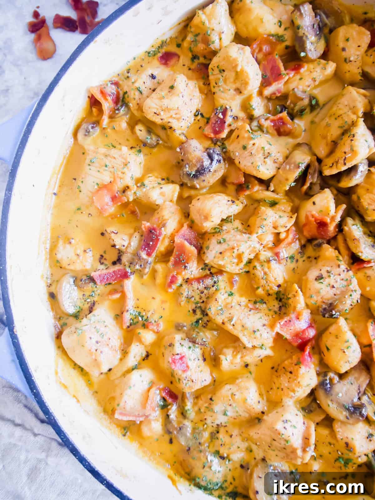 Rich coconut cream and chicken sauce with sautéed mushrooms and bacon pieces in a pan.