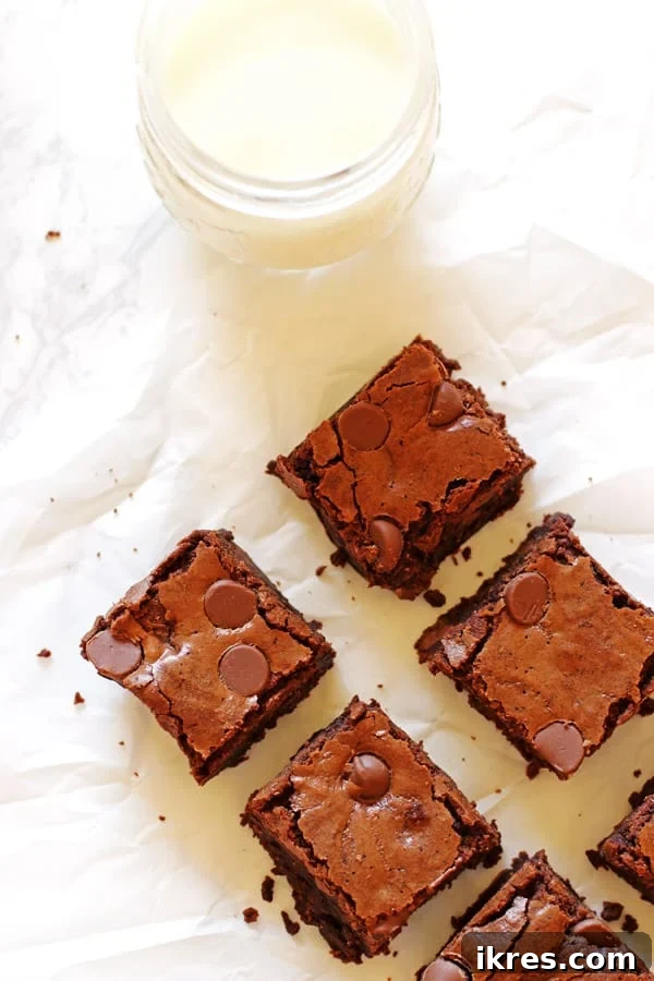Ultimate Homemade Brownies 3 Perfectly cut homemade brownies on white parchment paper, with a glass jug of milk in the background.
