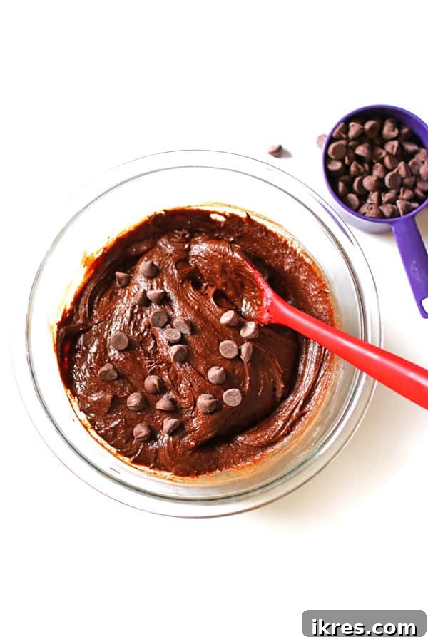 Ultimate Homemade Brownies 6 Brownie batter in a clear mixing bowl, with chocolate chips being folded into the rich chocolate mixture.