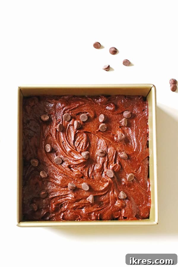 Ultimate Homemade Brownies 7 Unbaked brownie batter in a square baking pan, topped with extra chocolate chips, ready for the oven.