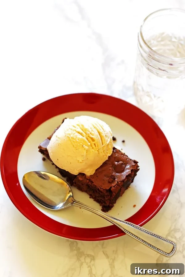Ultimate Homemade Brownies 9 A warm brownie on a red and white plate, topped with a scoop of melting vanilla ice cream, creating a simple brownie sundae.