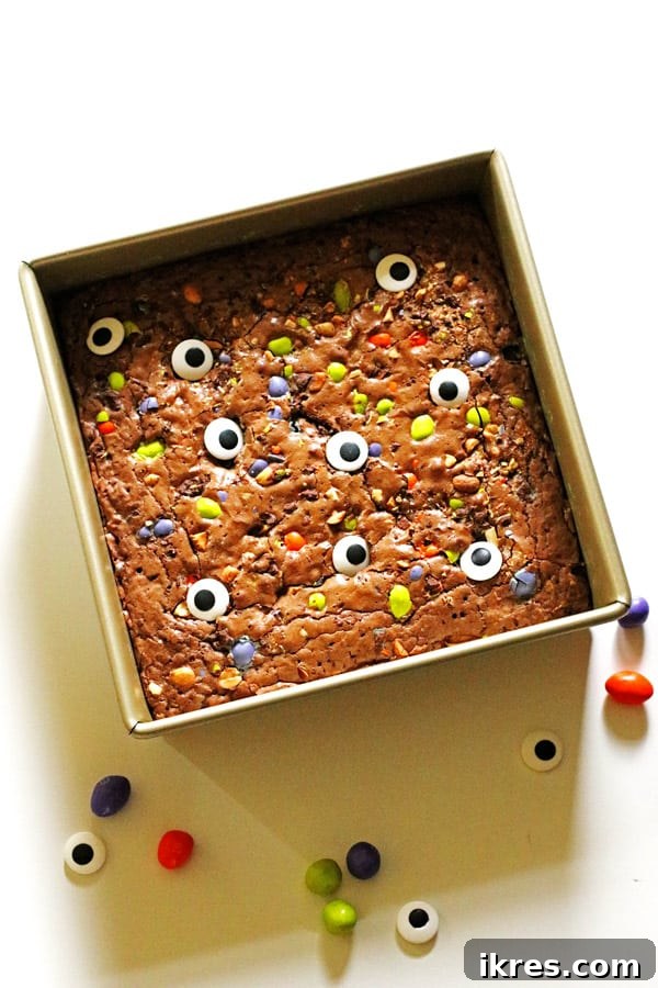Ultimate Homemade Brownies 10 Halloween brownies in a square pan, decorated with crushed colorful candies and edible candy eyes, ready for a party.