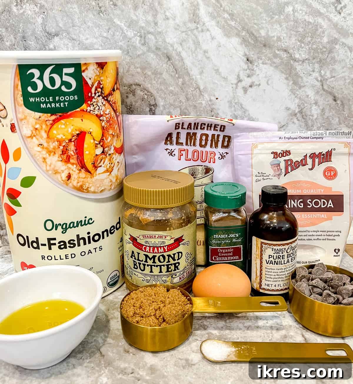 Wholesome Gluten Free Dairy Free Almond Oatmeal Treats 4 A collection of ingredients neatly laid out on a table, including rolled oats, almond flour, brown sugar, baking soda, cinnamon, an egg, almond butter, olive oil, vanilla extract, and dairy-free chocolate chips.