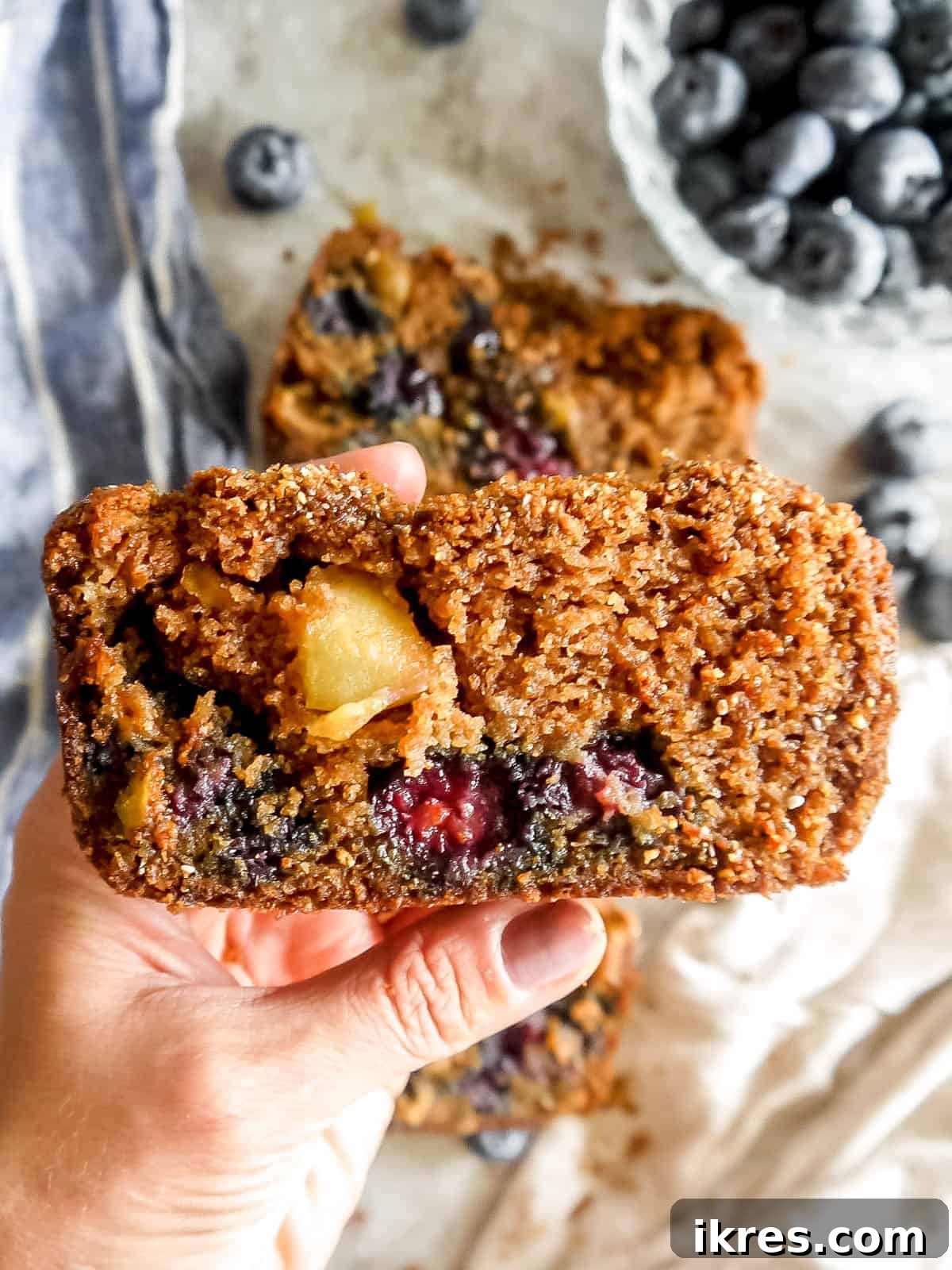 A slice of Healthy Apple Blueberry Bread in one's hands, showcasing its crumbly topping and fruit chunks.