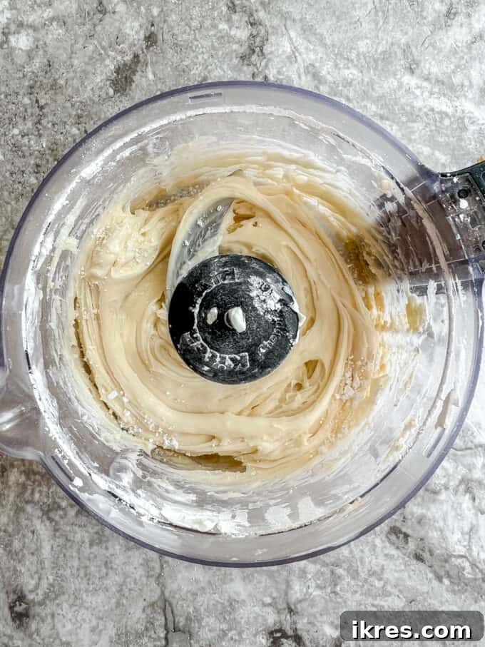 Artisanal Pumpkin Olive Oil Cake 11 Cream cheese frosting being blended to a smooth consistency in a food processor, highlighting its readiness for the cake.