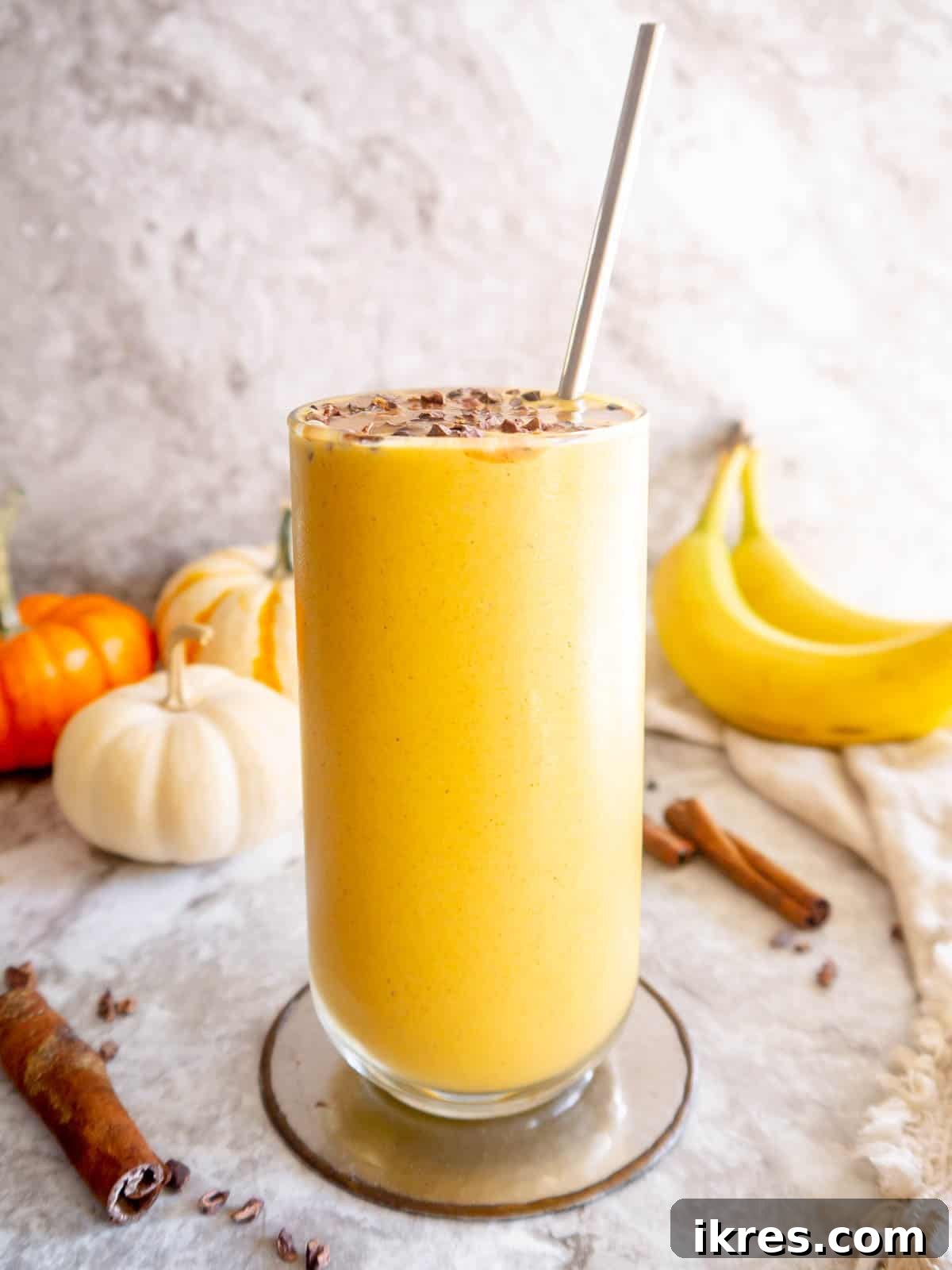 A beautifully composed shot of a Pumpkin Banana Smoothie in a glass, with fresh pumpkins and bananas artfully arranged in the background, highlighting the natural ingredients.