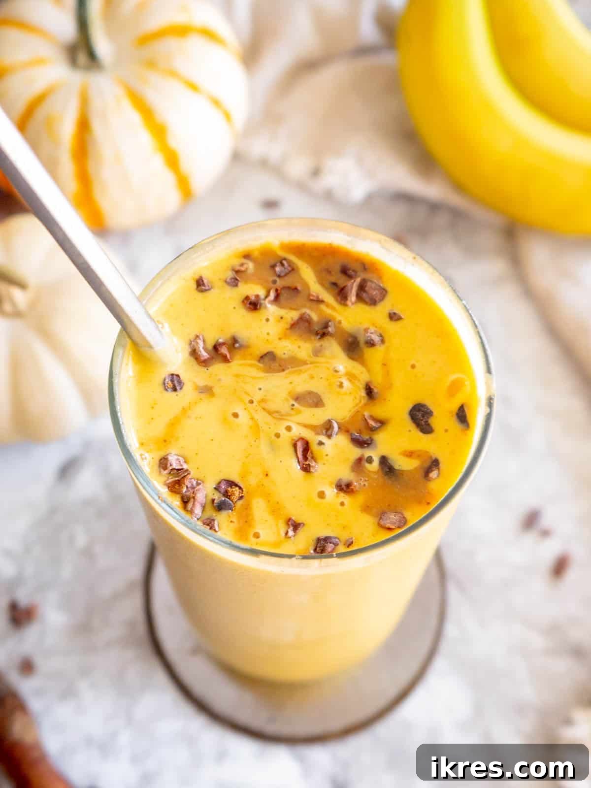 A close-up shot of a creamy Pumpkin Spice Smoothie with banana, generously mixed with crunchy cacao nibs, highlighting its rich texture and delicious additions.