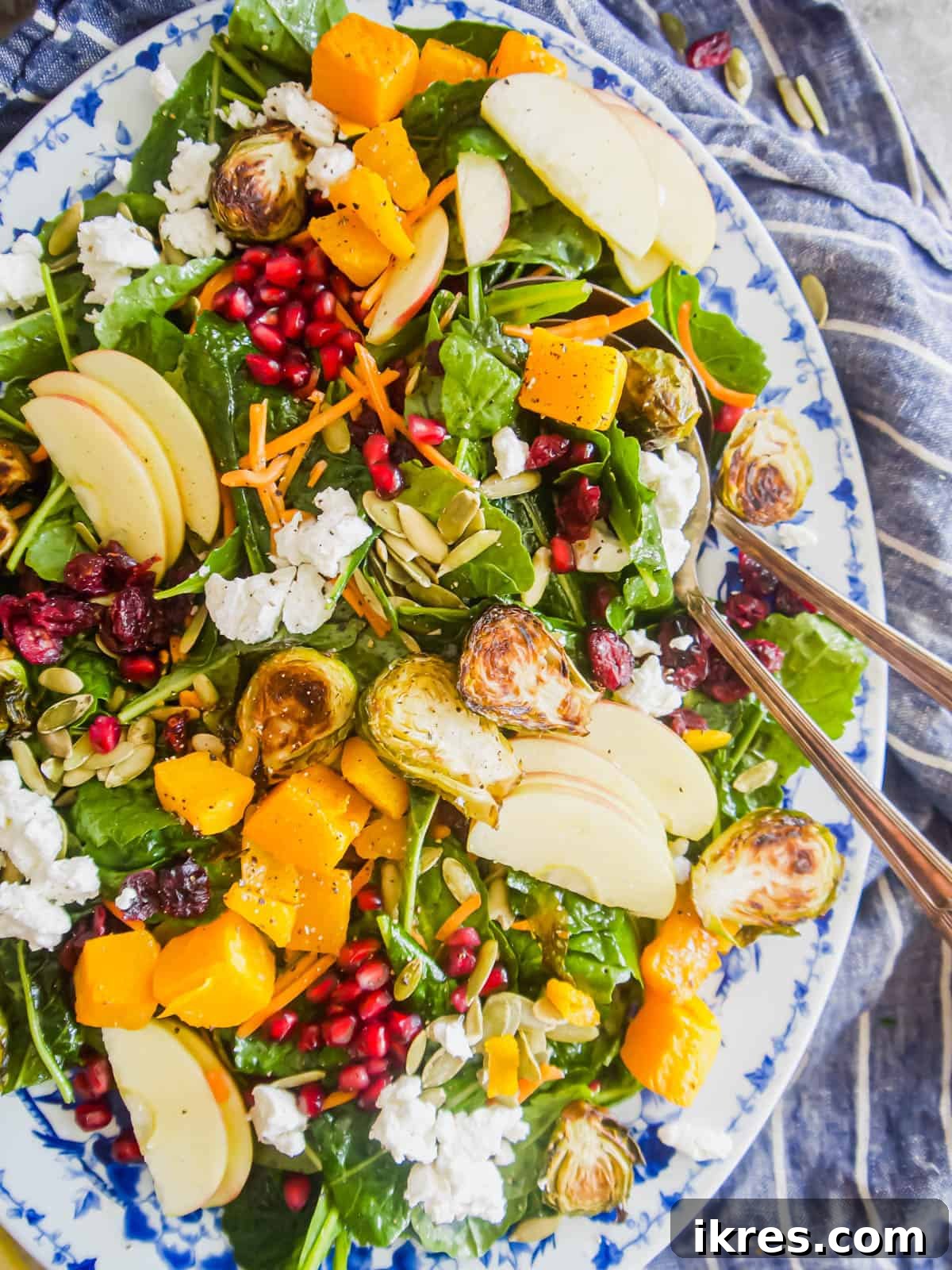 A beautifully arranged Fall Harvest Salad in a large serving bowl, featuring colorful roasted vegetables, fresh greens, and a hint of a large serving spoon.