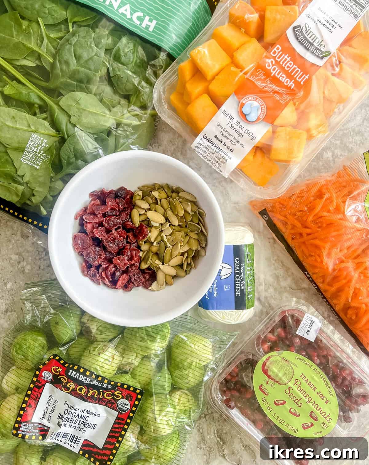 A vibrant display of fresh Fall harvest salad ingredients laid out on a white surface, showcasing butternut squash, Brussels sprouts, kale, and more.