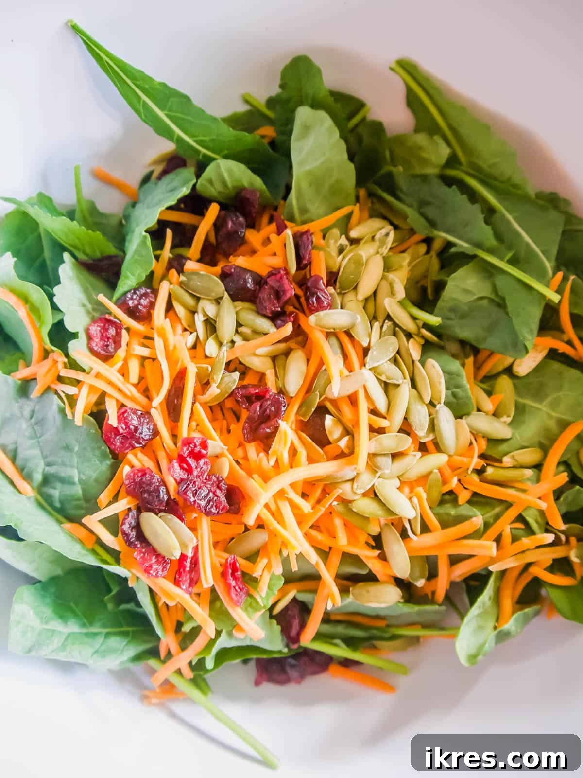 Fresh kale, shredded carrots, and pumpkin seeds tossed together in a large mixing bowl.