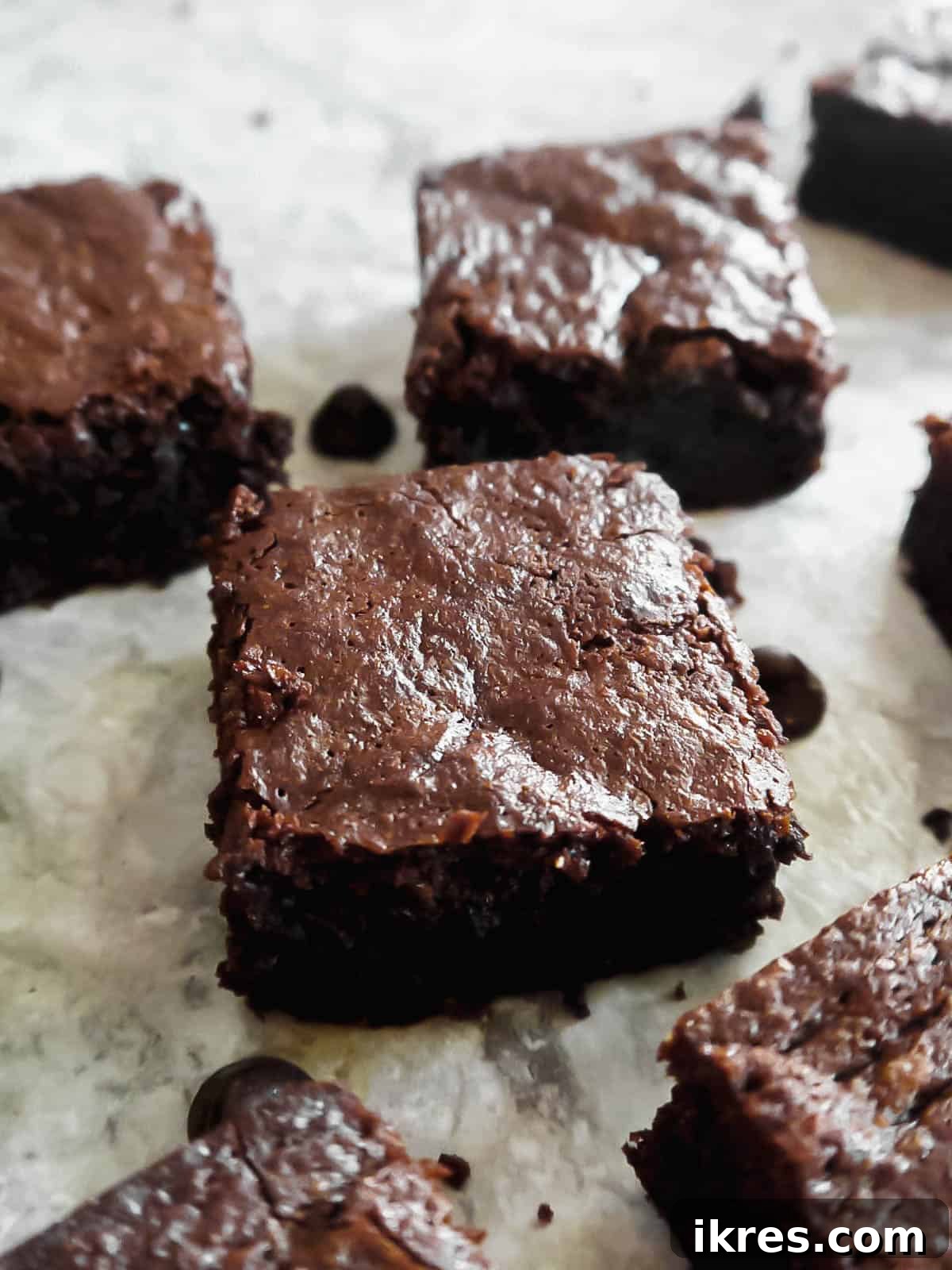 Deliciously Wholesome Almond Flour Brownies 3 Slices of rich olive oil brownies with an assortment of dairy-free chocolate chips scattered beside them.