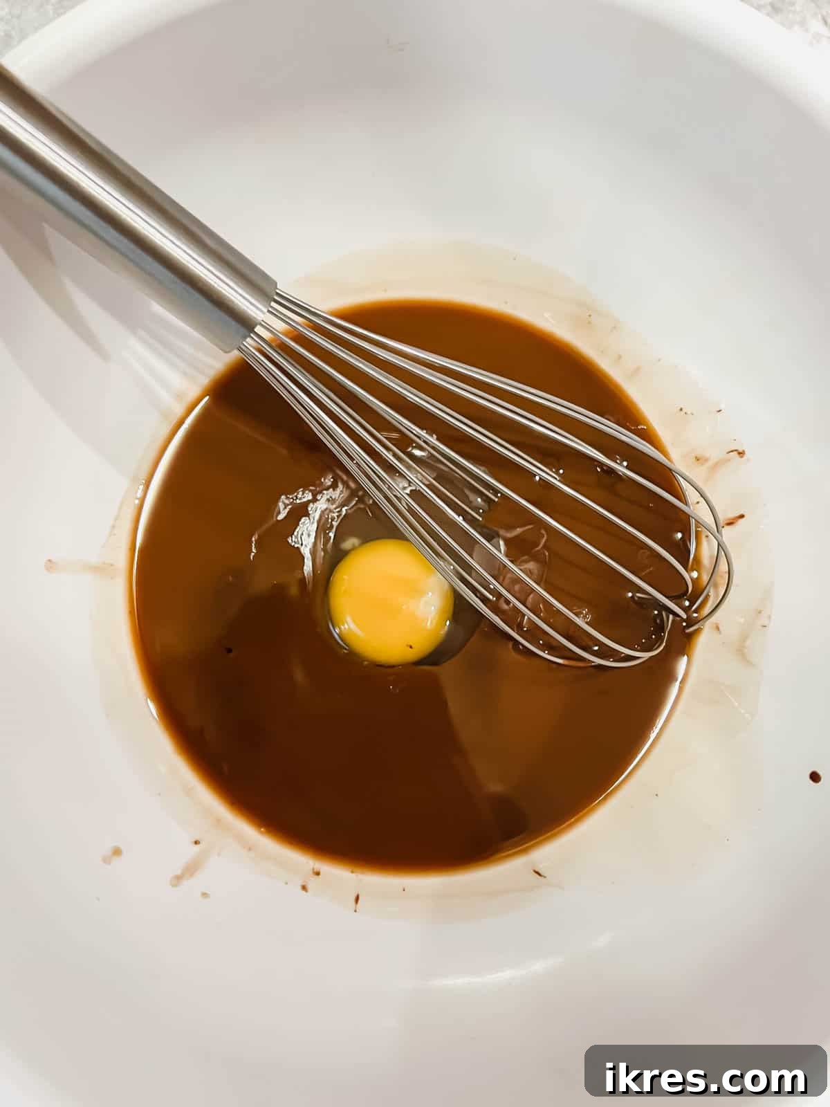 Deliciously Wholesome Almond Flour Brownies 7 A whisk incorporating a single egg into the chocolate brownie batter in a bowl.