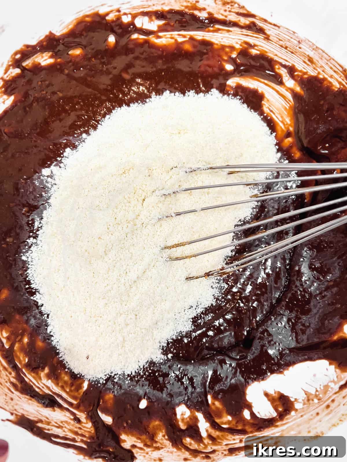 Deliciously Wholesome Almond Flour Brownies 9 Dry almond flour mixture being poured into the wet chocolate batter in a mixing bowl.