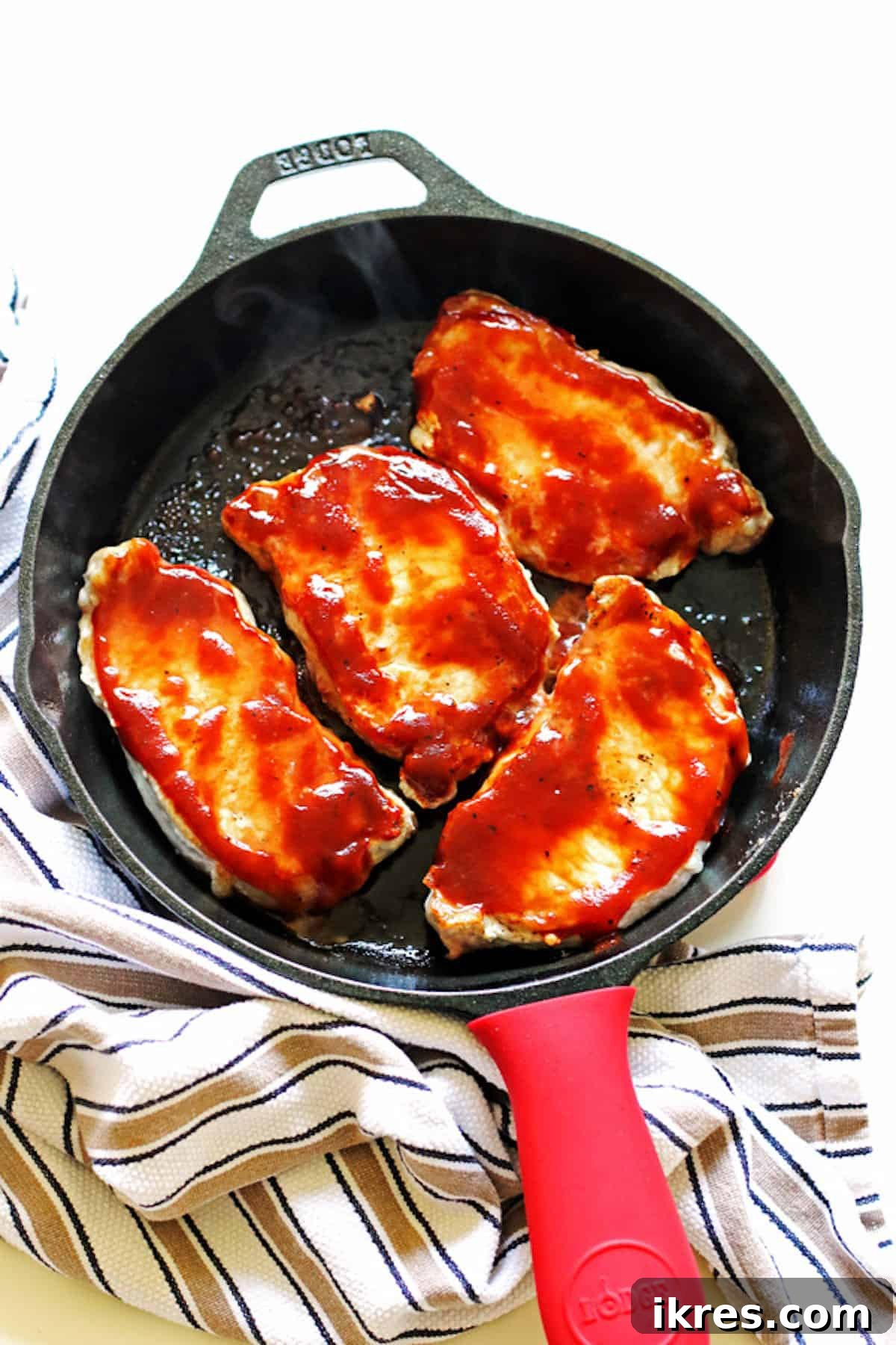 Smoky Grilled Pork Chops 2 A cast iron pan with four perfectly cooked, glistening barbecue pork chops.