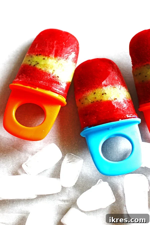 Refreshing Fruit Freezes 3 Fruit Popsicles on a white counter with ice cubes laying next to them
