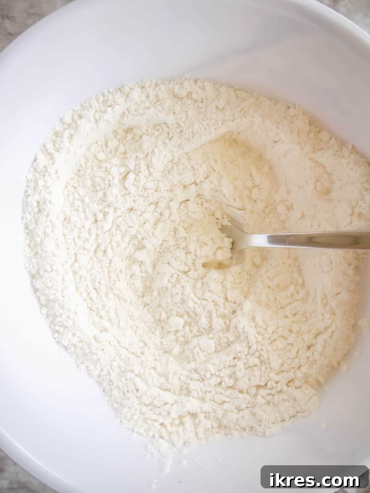 Dry ingredients like flour, baking powder, baking soda, and salt mixed in a bowl with a fork.