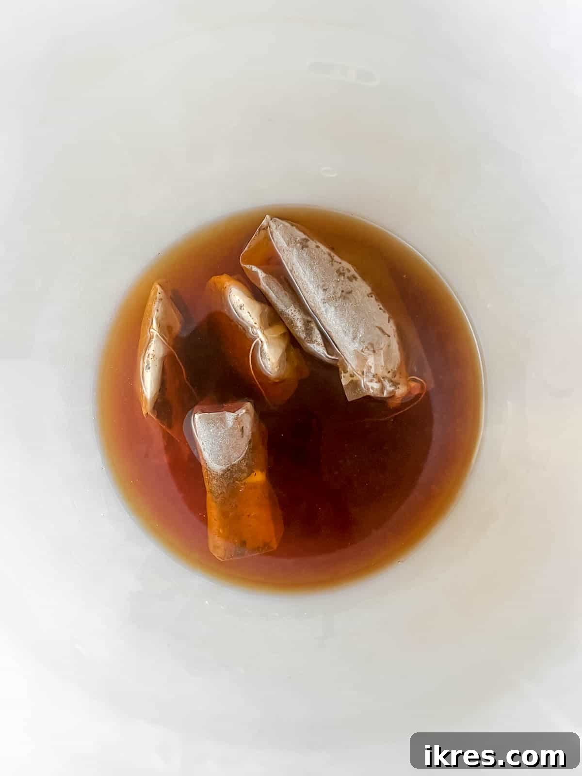 Black tea bags steeping in hot water in a large pitcher.