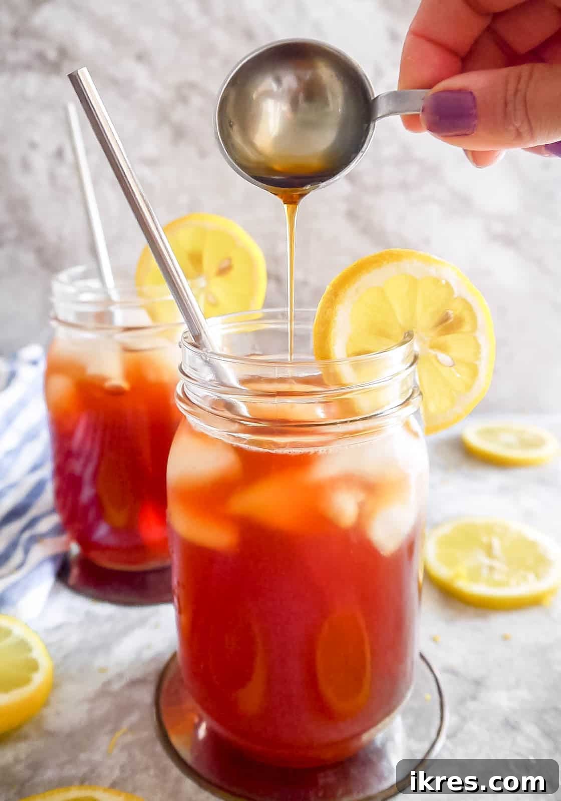 Healthy sweet tea in two cups, with a bottle of maple syrup being poured into one cup.