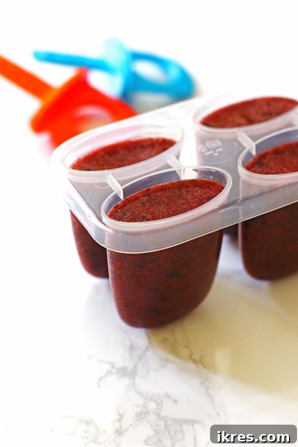 Blueberry lemon popsicle mixture freshly poured into individual popsicle molds, ready for the freezer.