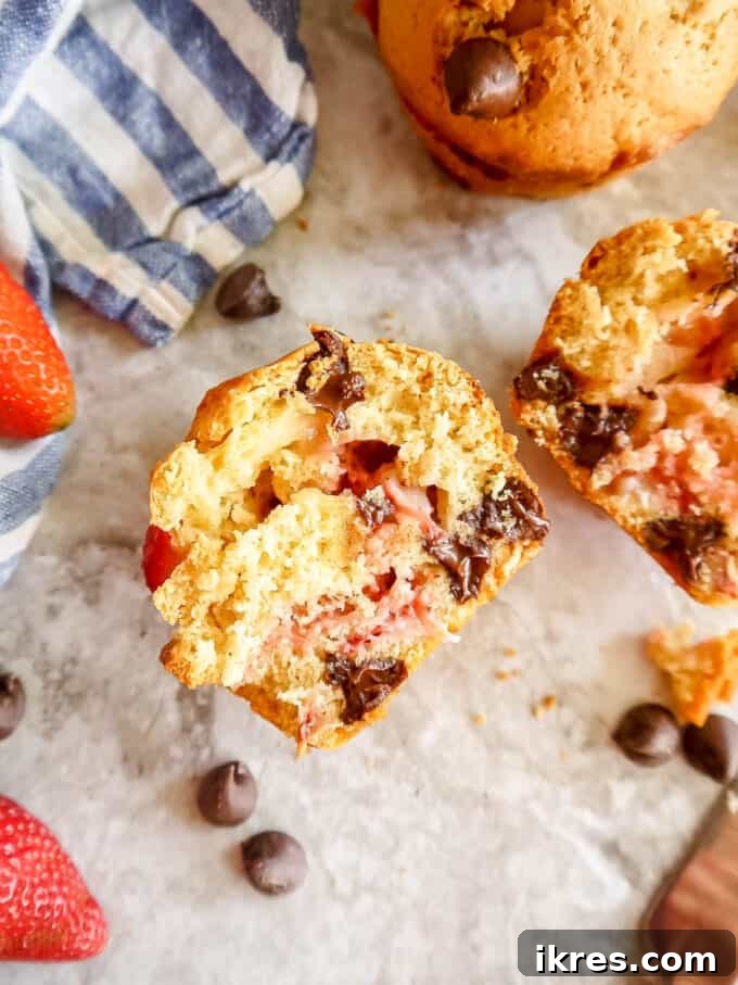 A strawberry chocolate chip muffin cut in half, revealing the soft interior with pockets of melted chocolate and vibrant strawberry pieces
