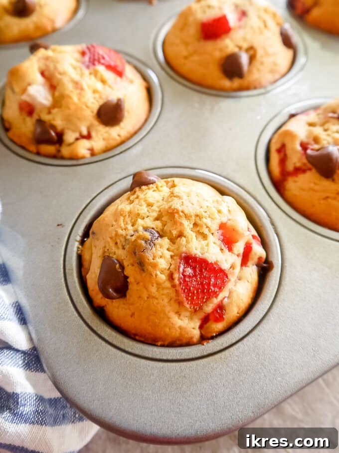 side angle of strawberry muffins in a tin pan, with one muffin removed