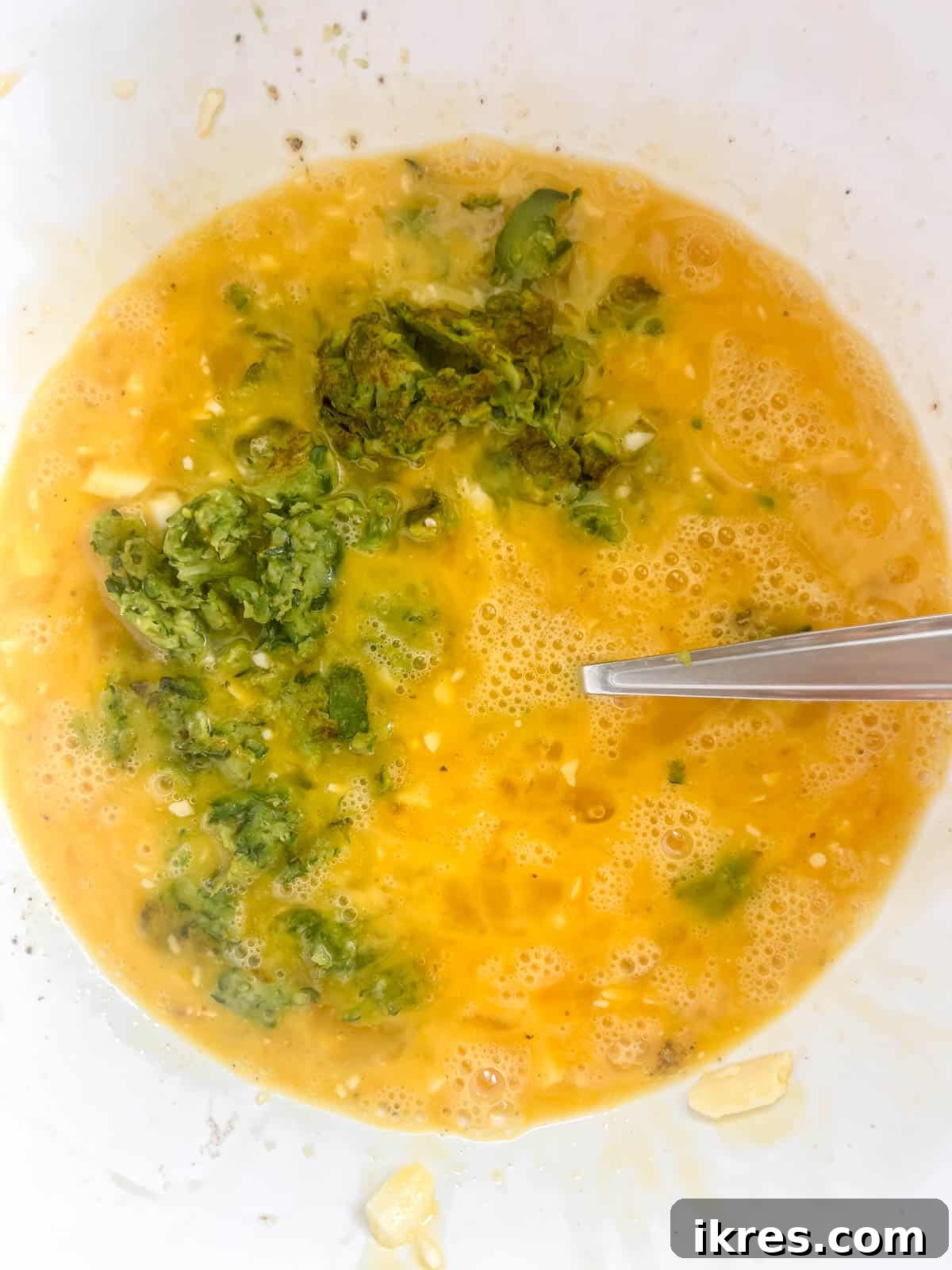 Zucchini added to the eggs in a bowl.