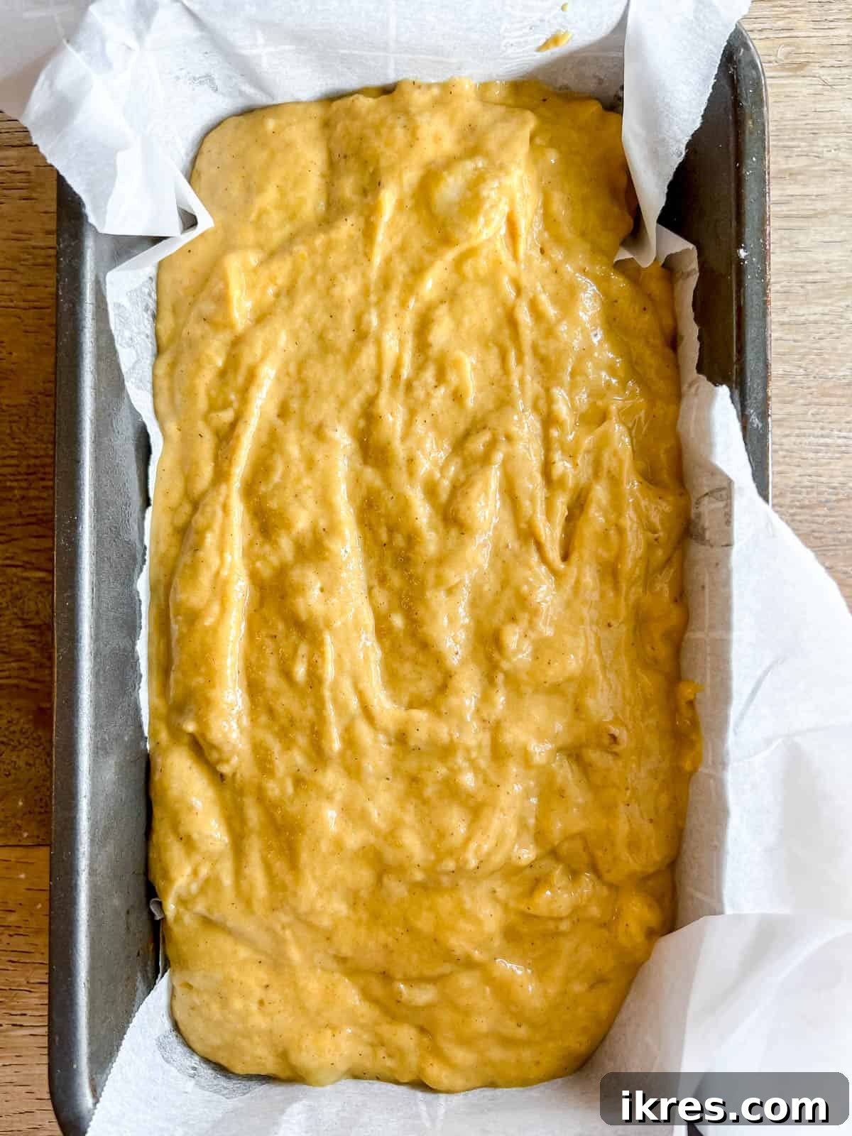 Pumpkin banana bread batter poured into a parchment-lined loaf tin, ready for baking.