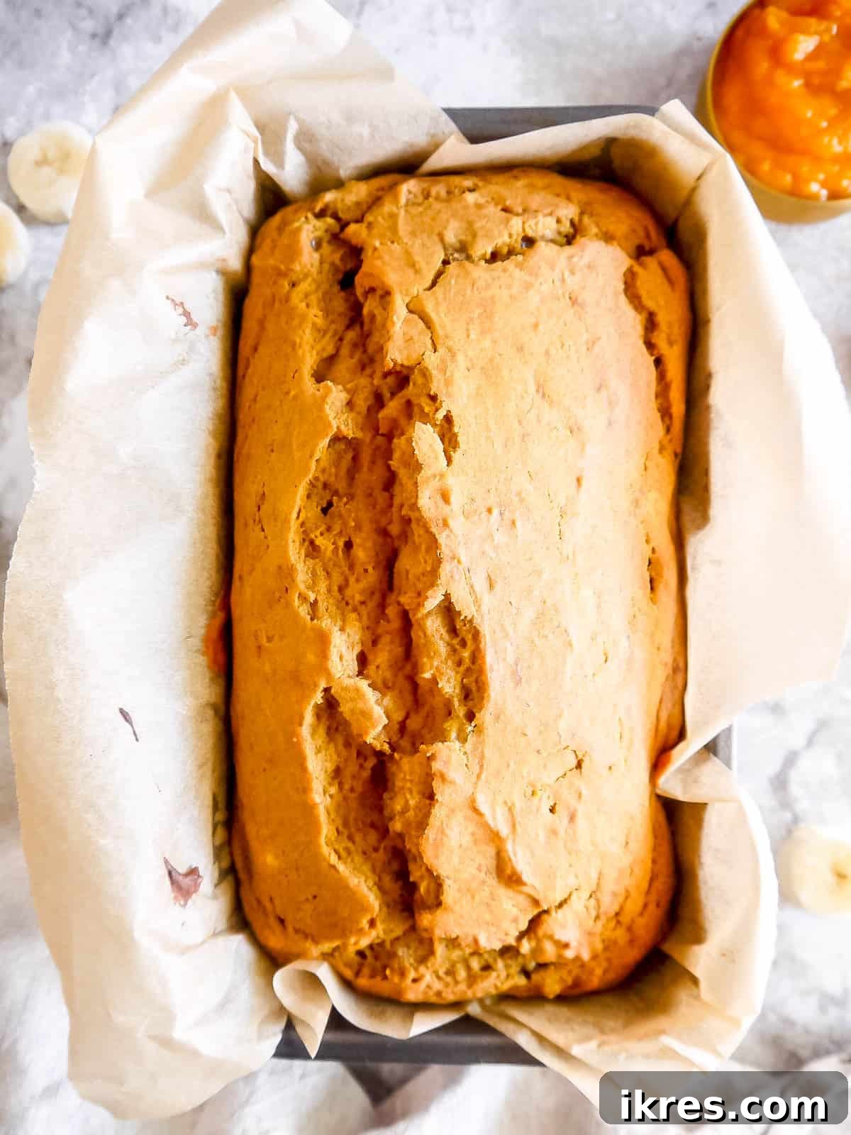 A freshly baked loaf of golden-brown pumpkin banana bread cooling in the pan.