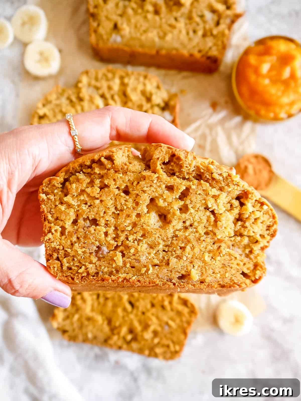 A hand holding a perfectly sliced piece of banana pumpkin bread, ready to be eaten.