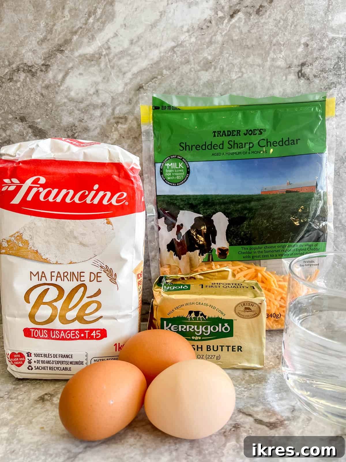 Gougères: Golden Clouds of Cheesy Delight 3 A flat lay photograph showing the simple ingredients required to make Gougères: a stick of butter, a bowl of flour, eggs, and a pile of shredded Gruyère cheese.