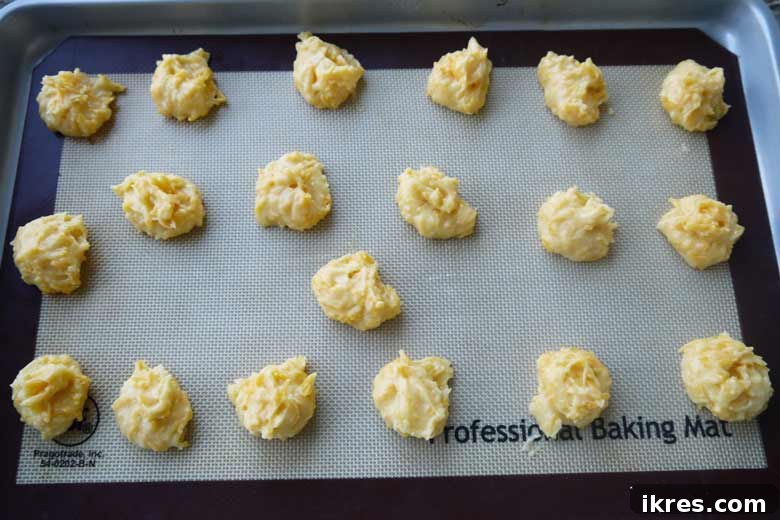 Gougères: Golden Clouds of Cheesy Delight 6 Unbaked Gougères batter spooned onto a parchment-lined baking sheet, ready for the oven.