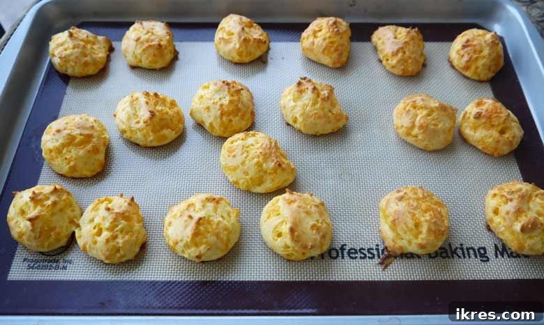 Gougères: Golden Clouds of Cheesy Delight 7 Freshly baked Gougères, golden brown and perfectly puffed, on a baking sheet immediately after baking.