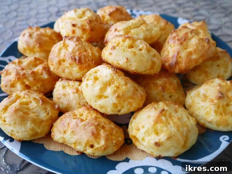 Gougères: Golden Clouds of Cheesy Delight 8 A stack of perfectly golden and puffed Gougères arranged artfully on a white plate, ready to be served as an elegant appetizer.