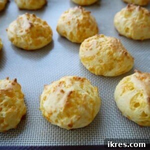 Gougères: Golden Clouds of Cheesy Delight 9 A close-up of a stack of golden brown Gougères, showcasing their puffed texture, on a white plate with a dark background.