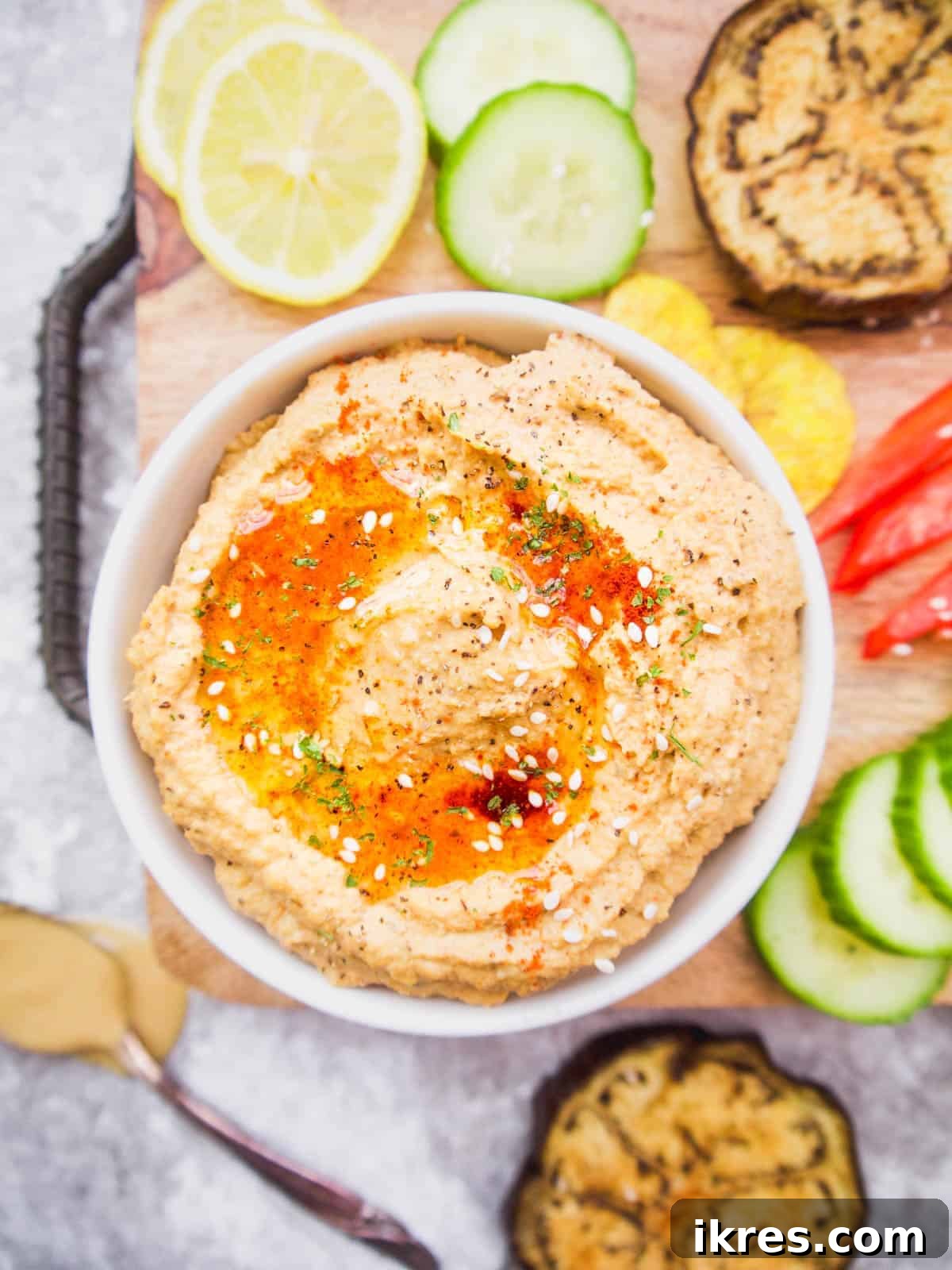 Creamy cauliflower hummus in a rustic bowl, garnished with roasted eggplant and red peppers, ready to be served.