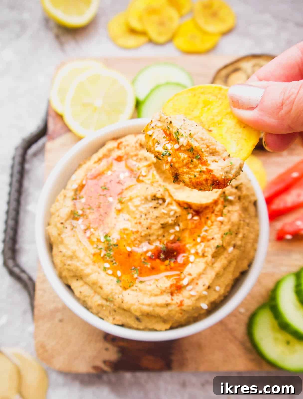A spoonful of Mediterranean Cauliflower Hummus being lifted from a bowl with a plantain chip, showcasing its creamy texture.
