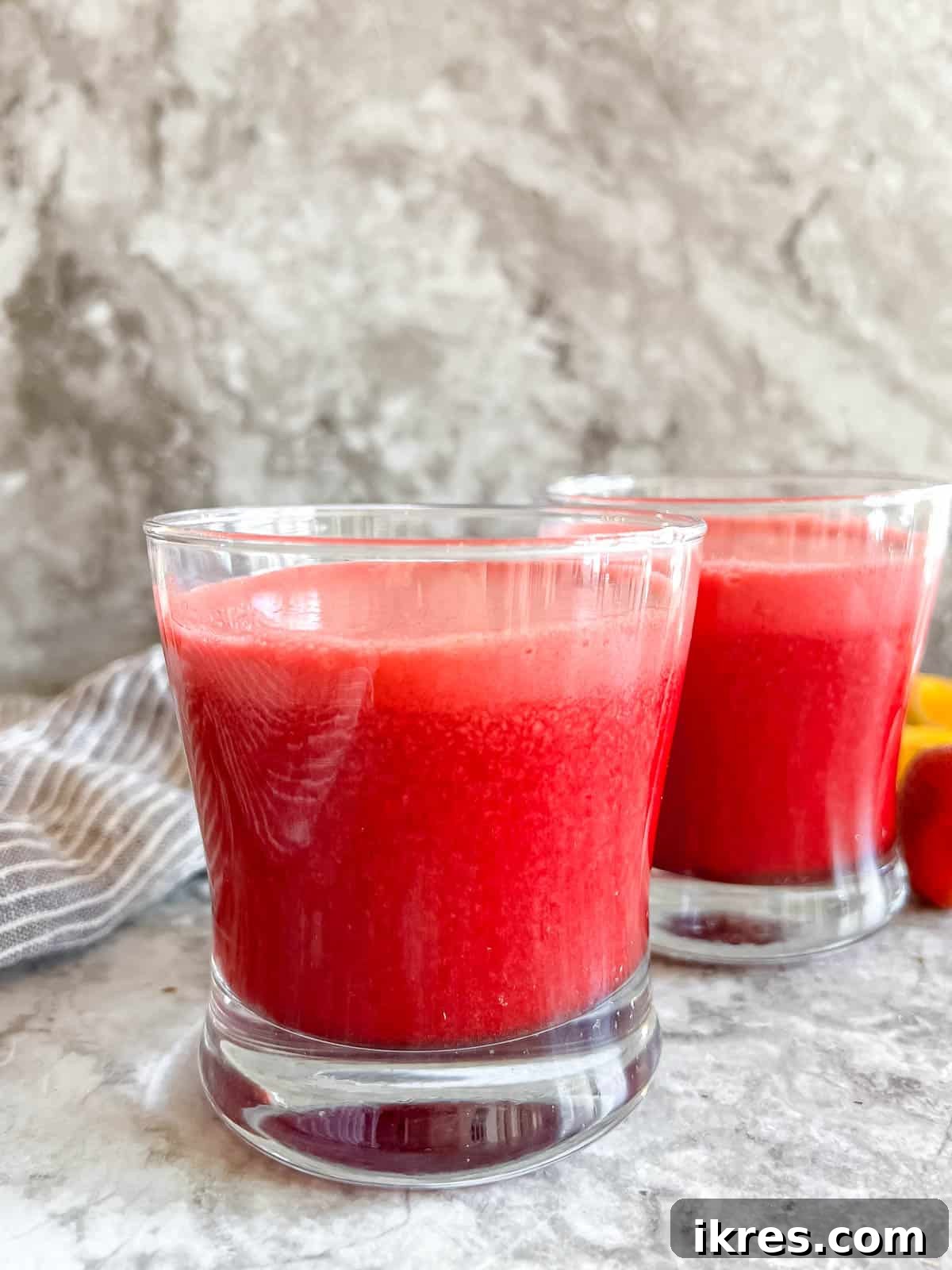 Vibrant Root Nectar 5 Two glasses of strawberry, beetroot, and carrot juice garnished with oranges and strawberries, on a rustic background.