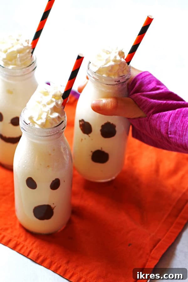 Monster Milkshake Creations 5 A finished Halloween Ghost Milkshake in a clear glass, featuring a creamy vanilla milkshake base, chocolate ghost face, and a swirl of whipped cream on top.