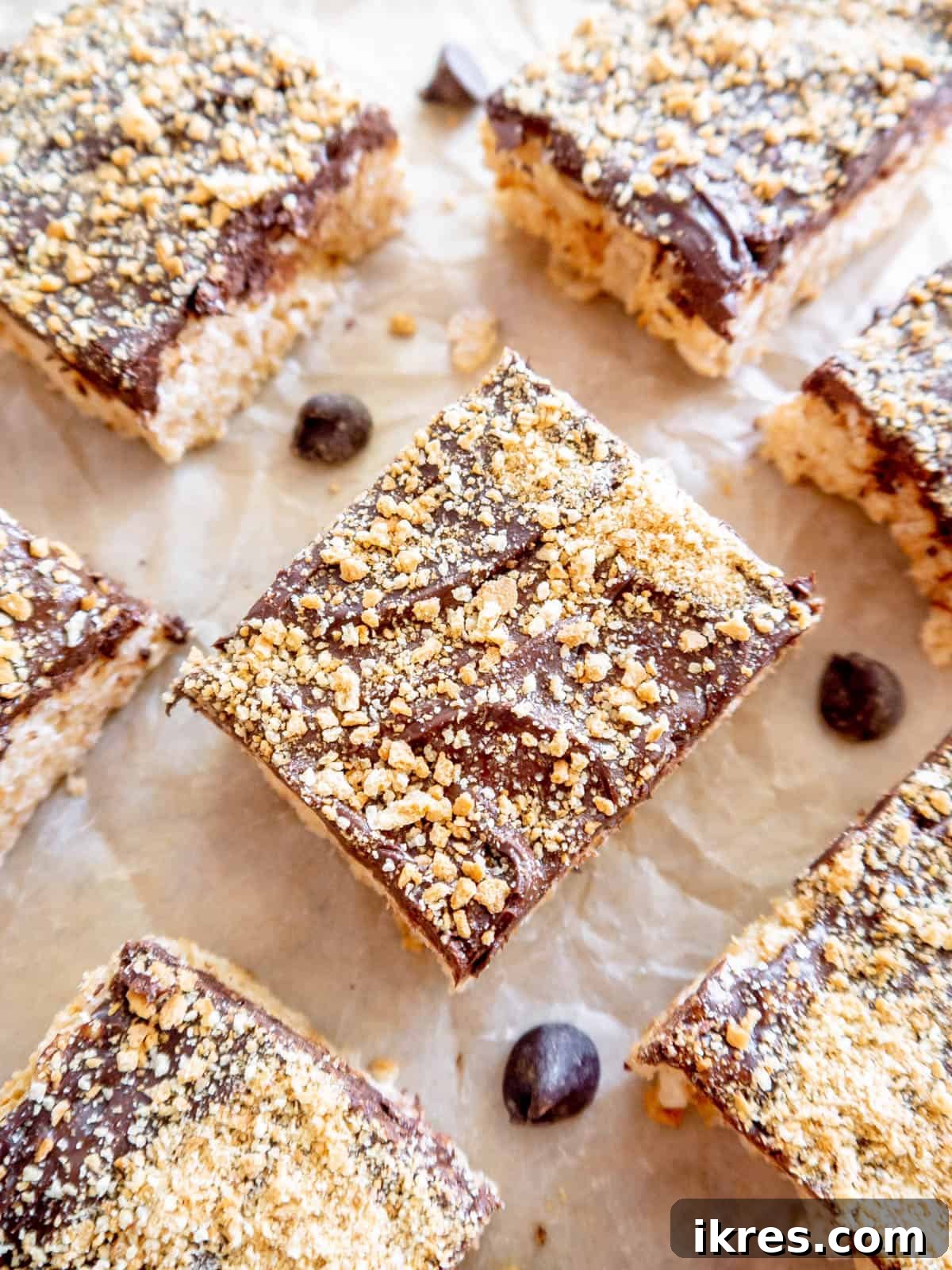 Golden brown S'mores Rice Krispie Treats, perfectly cut into squares and arranged on parchment paper, showcasing the distinct layers of crispy cereal, chocolate, and graham cracker topping.
