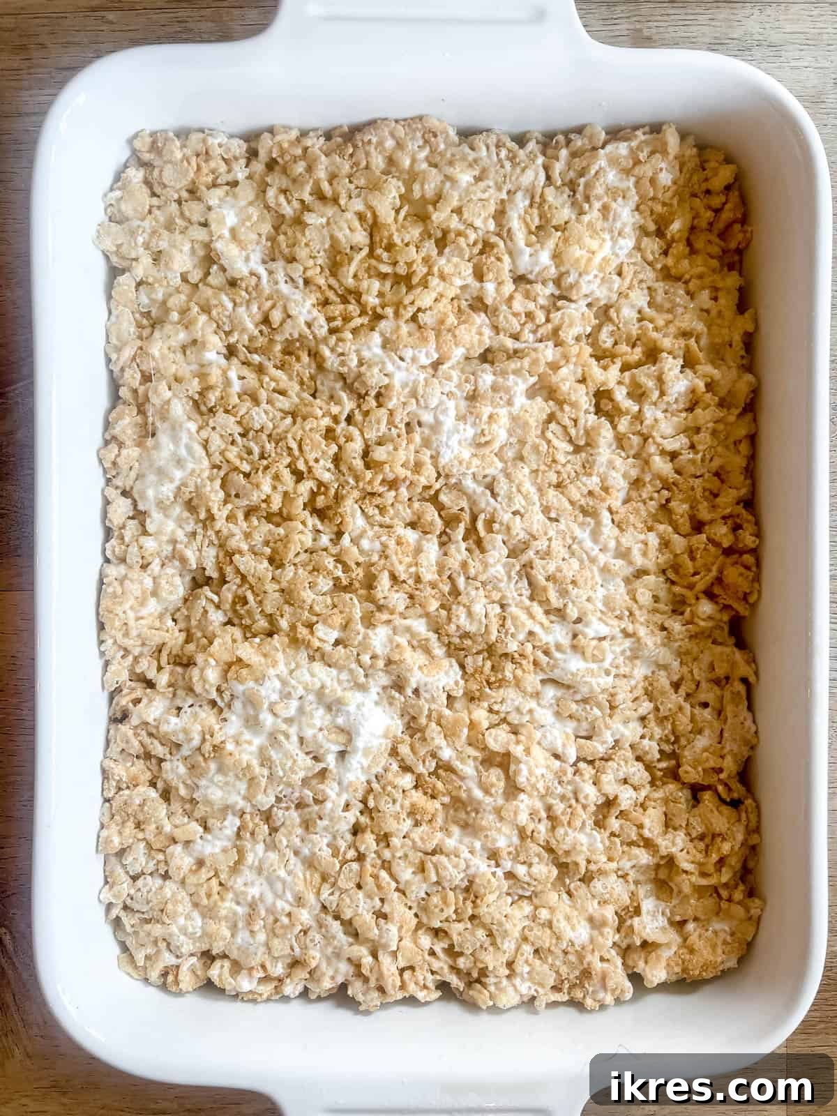 The S'mores Rice Krispie Treat mixture is pressed firmly and evenly into a greased baking pan, forming a flat and compact layer.