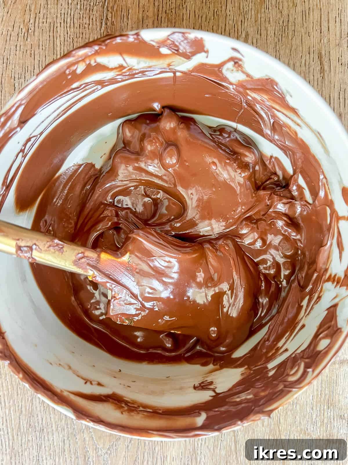 A bowl of smooth, glossy melted chocolate, perfectly ready to be spread over the S'mores Rice Krispie Treats.